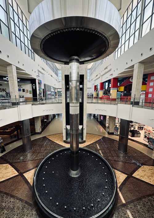 Free Wide shot of a modern mall interior featuring a central water fountain with geometric design. Stock Photo