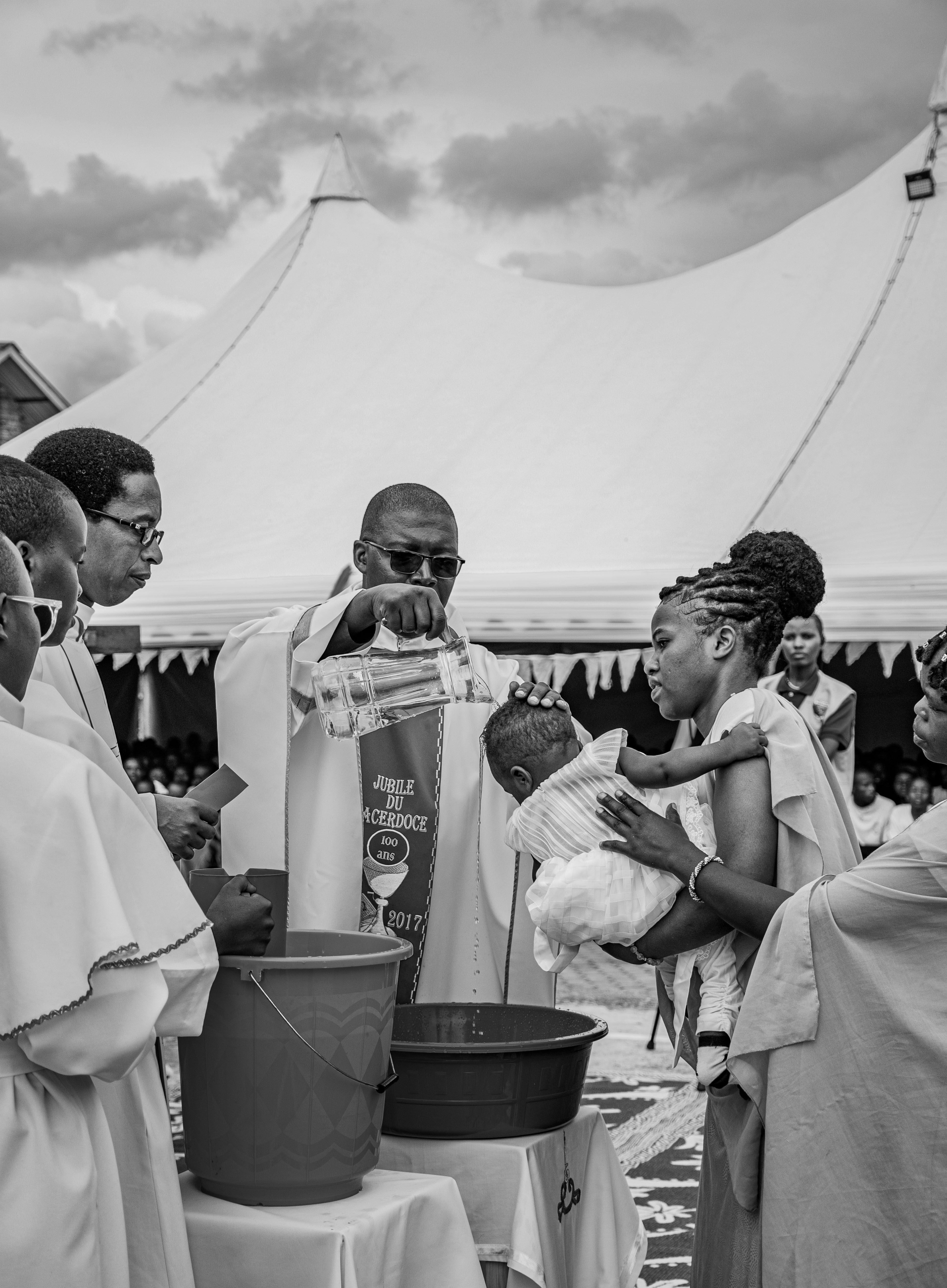 A priest performing a baptism ceremony outdoors under a tent