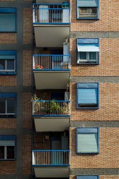 Brick apartment facade with balconies and blue window frames under the sunlight.