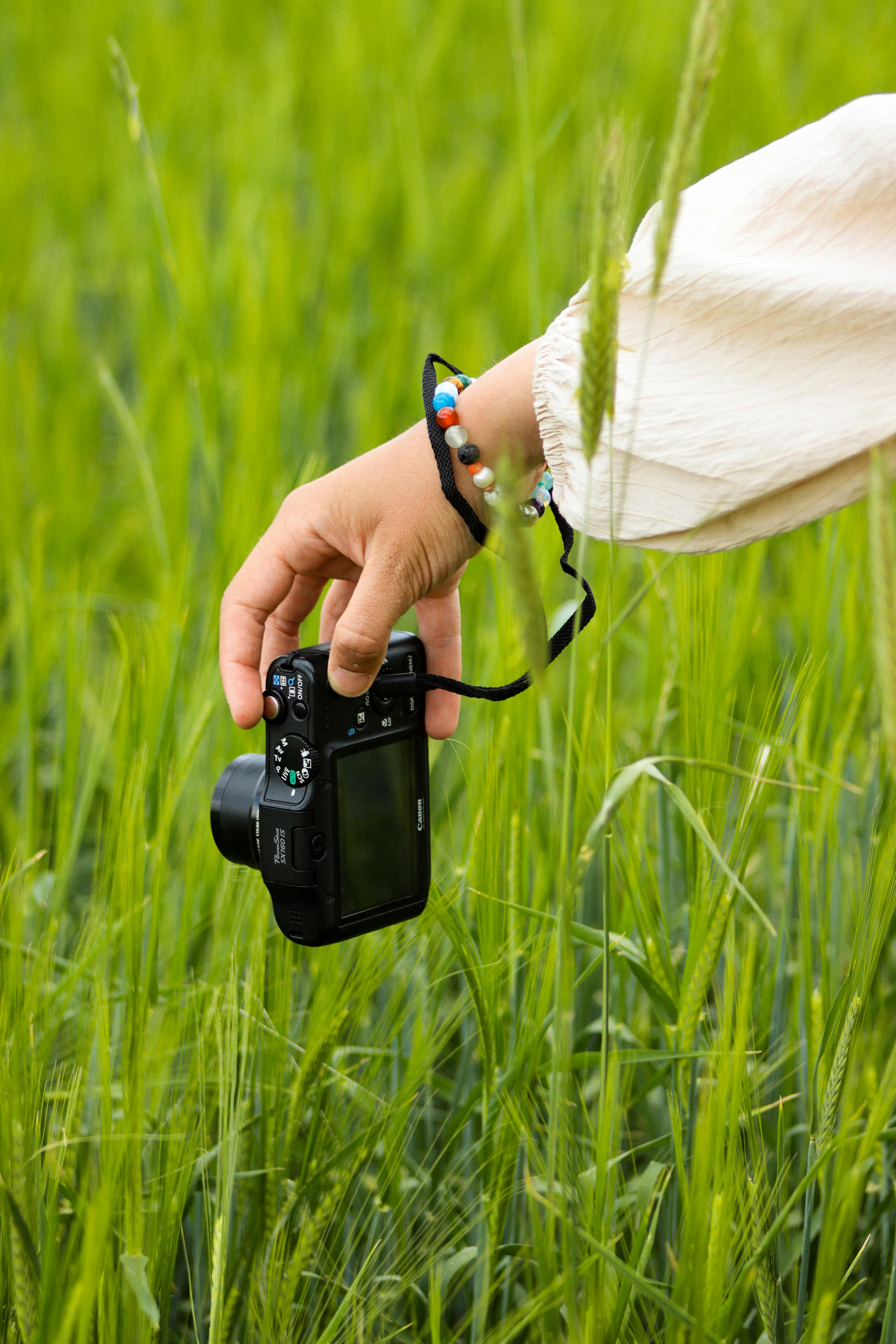 A photographer's hand holding a camera in a lush green field, capturing nature.