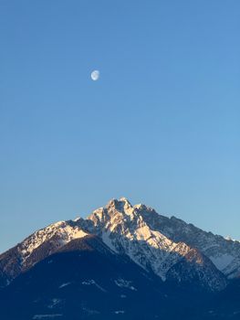 Scenic view of the Austrian Alps with snow under a clear sky and visible moon.