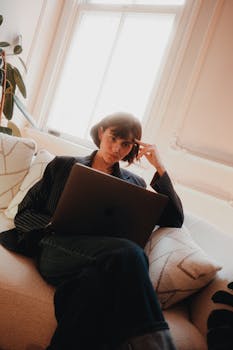 Woman in a cozy setting using a laptop, reflecting in a serene indoor atmosphere.