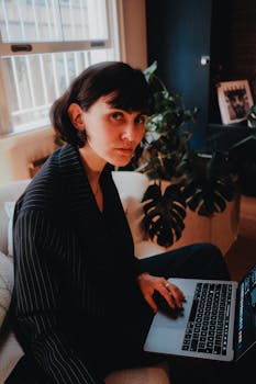 Stylish woman in striped suit working on laptop indoors with moody lighting.