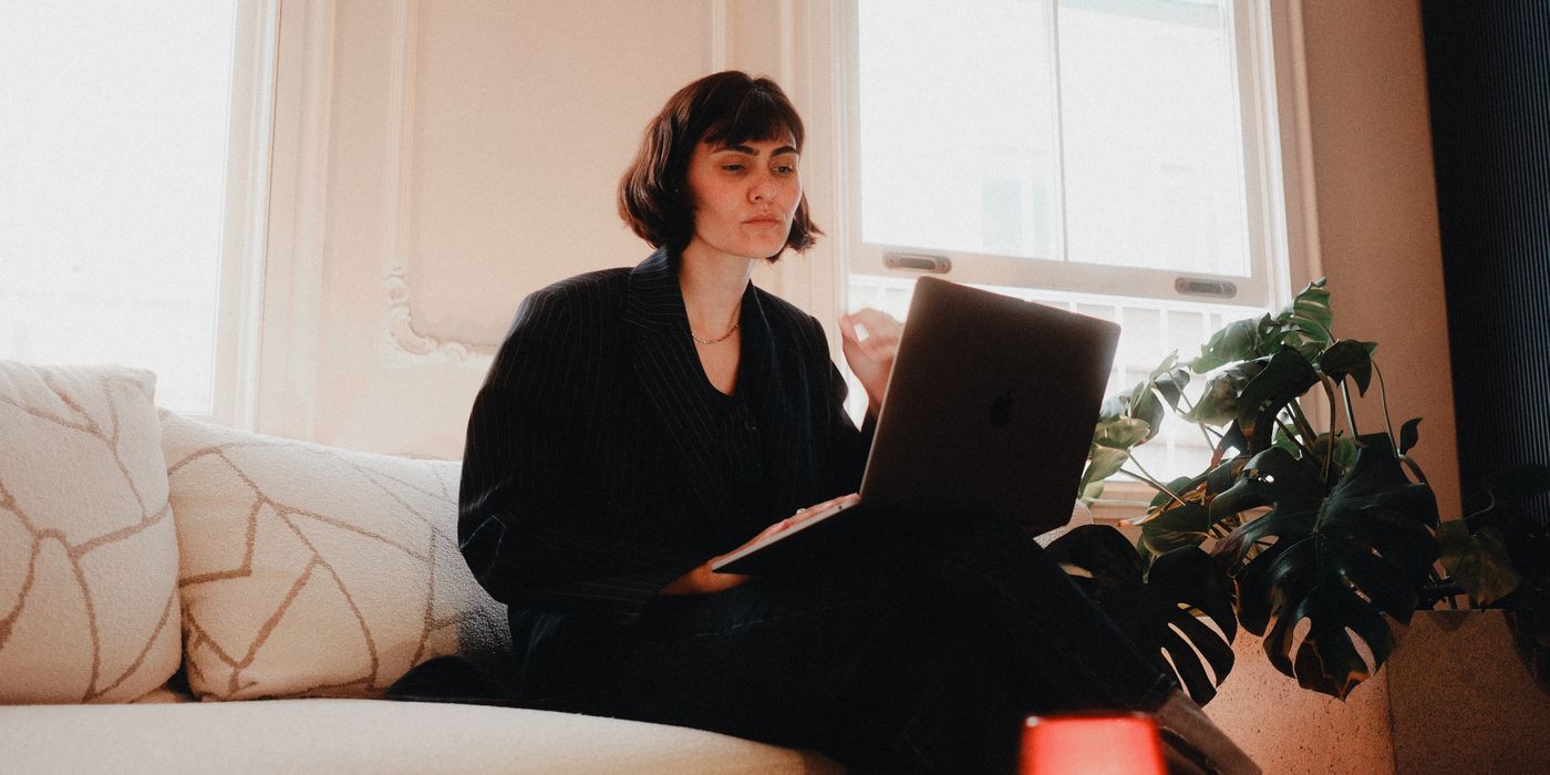 Woman in suit using laptop on sofa in bright room, modern lifestyle.
