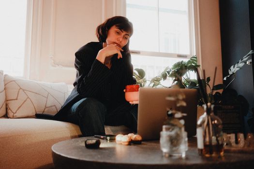 Woman contemplating at home with coffee mug and laptop on table. Cozy indoor setting.