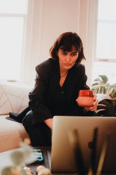 Focused woman in a home office setting with laptop and coffee mug, embodying remote work lifestyle.