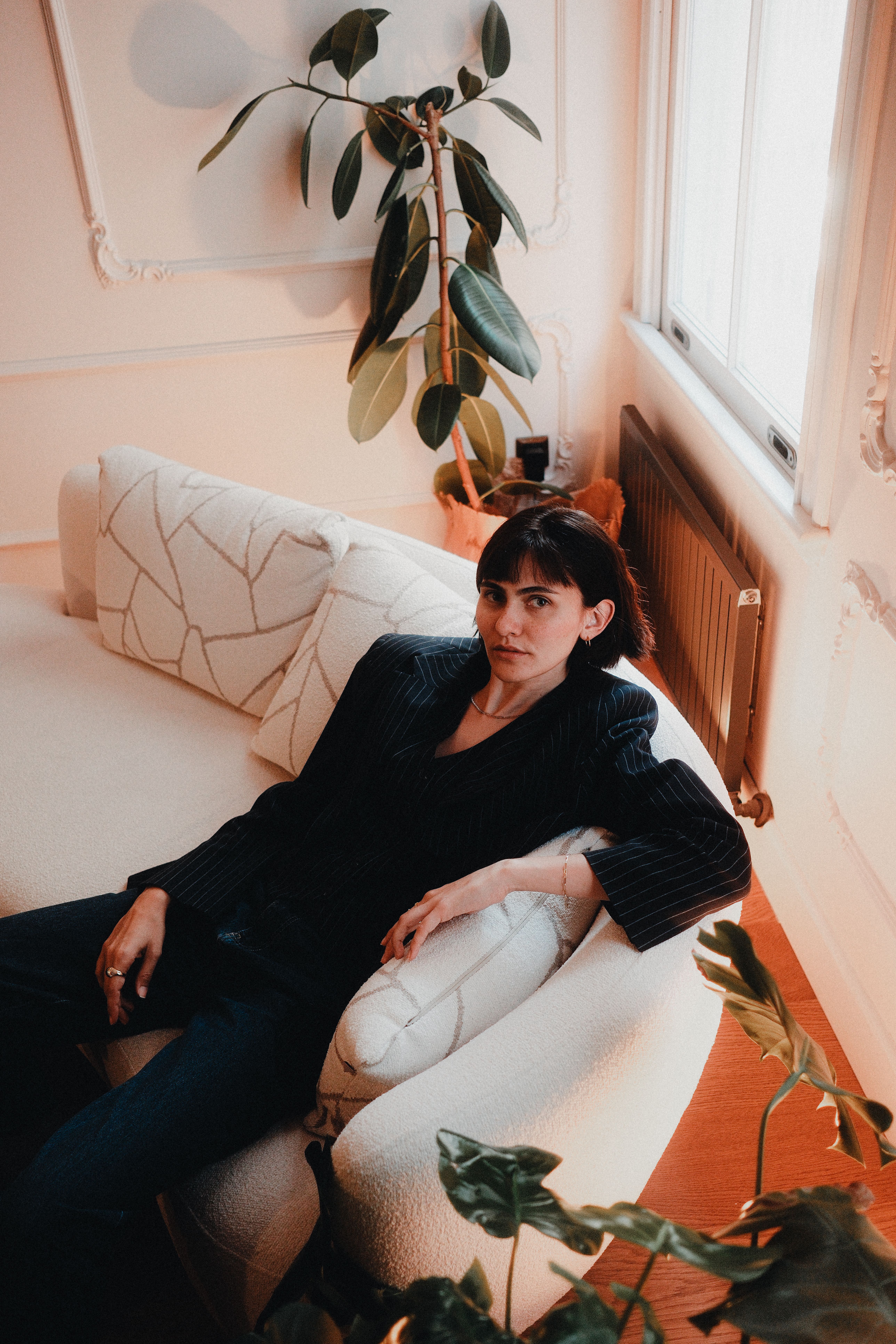 Elegant woman sitting on a modern sofa in a chic living room with plants.