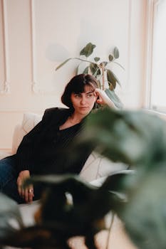 A woman in a black top sitting on a sofa, looking contemplative in a stylish interior.