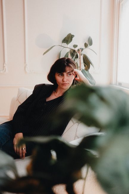 A woman in a black top sitting on a sofa, looking contemplative in a stylish interior.