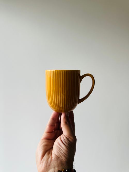 Free A minimalist photo of a yellow mug held by a hand against a neutral background. Stock Photo