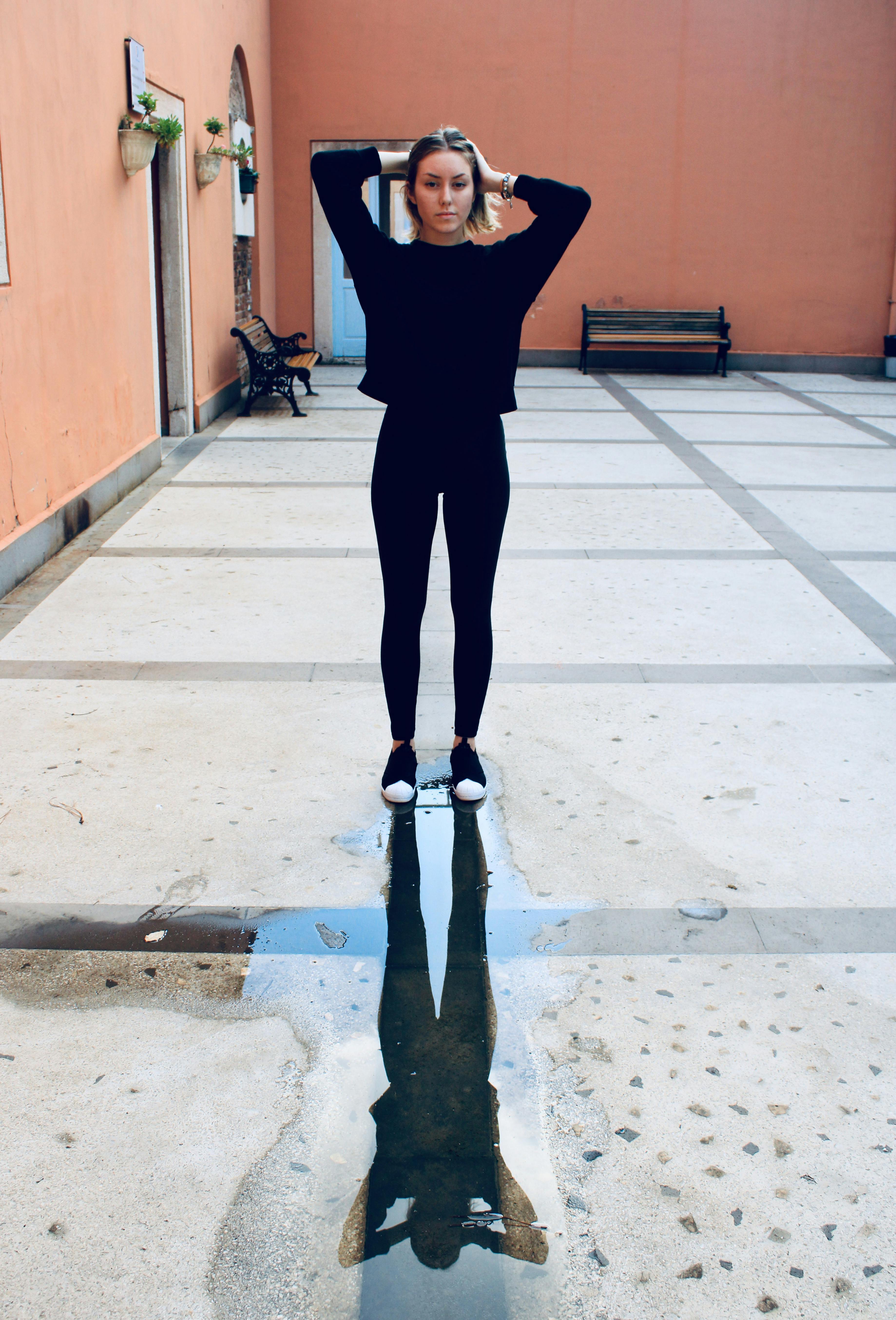 一位穿着休闲装的年轻女子站在院子里的反光水坑旁