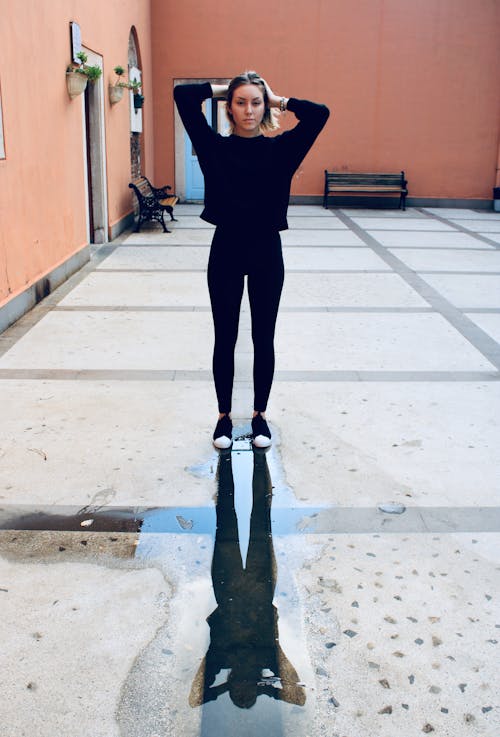 Woman Wearing Black Top and Black Pants Standing With Her Hands on Her Head