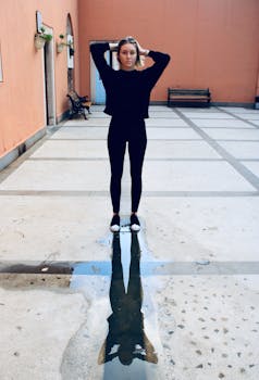 一位穿着休闲装的年轻女子站在院子里的反光水坑旁