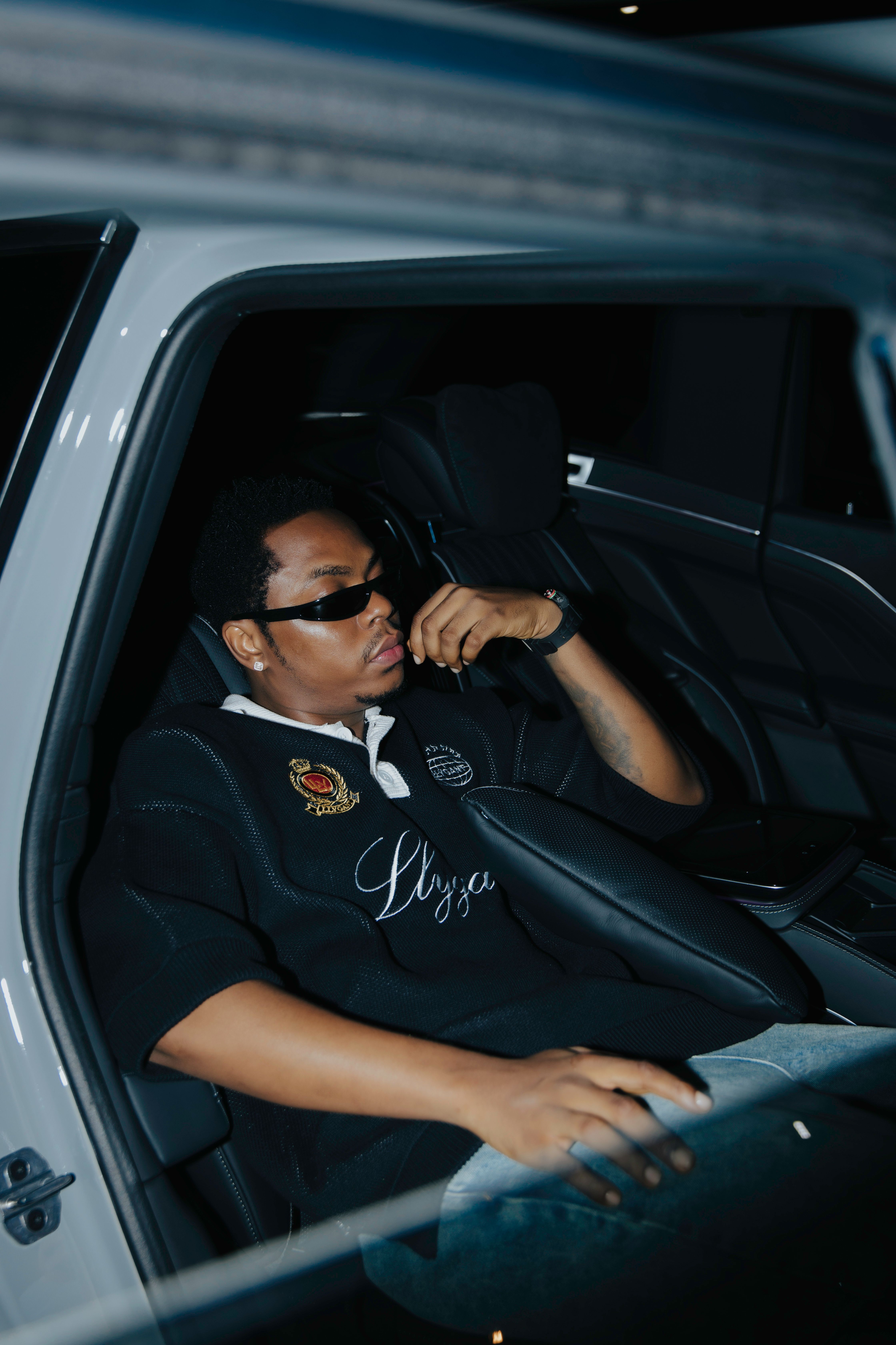 Man in a car wearing sunglasses and a black shirt, exuding style and confidence.