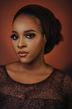 Elegant portrait of a woman wearing a brown headscarf and lace dress, highlighting beauty.