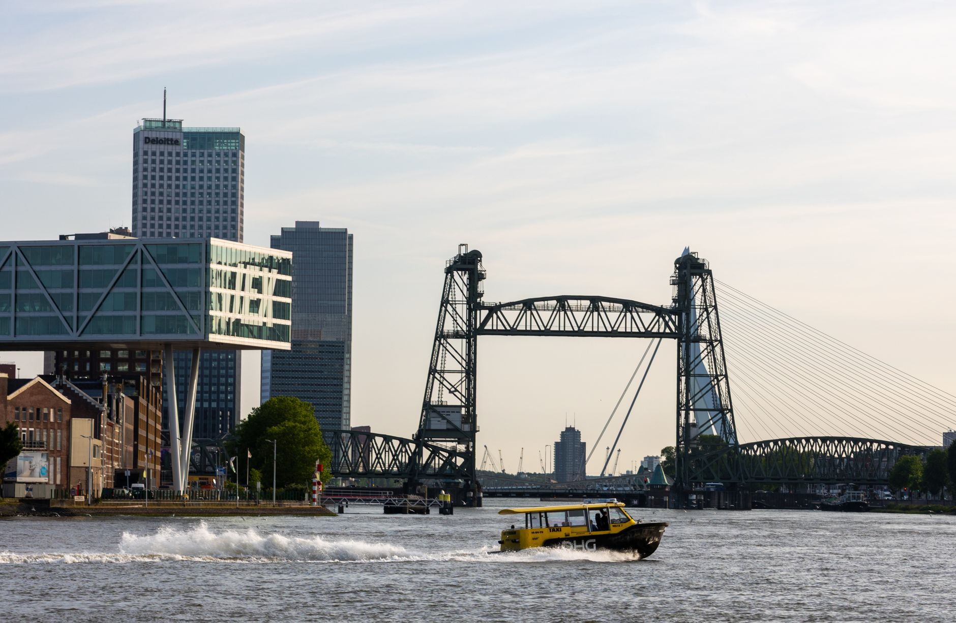 Explore the vibrant skyline of Rotterdam featuring De Hef and a yellow water taxi speeding by.
