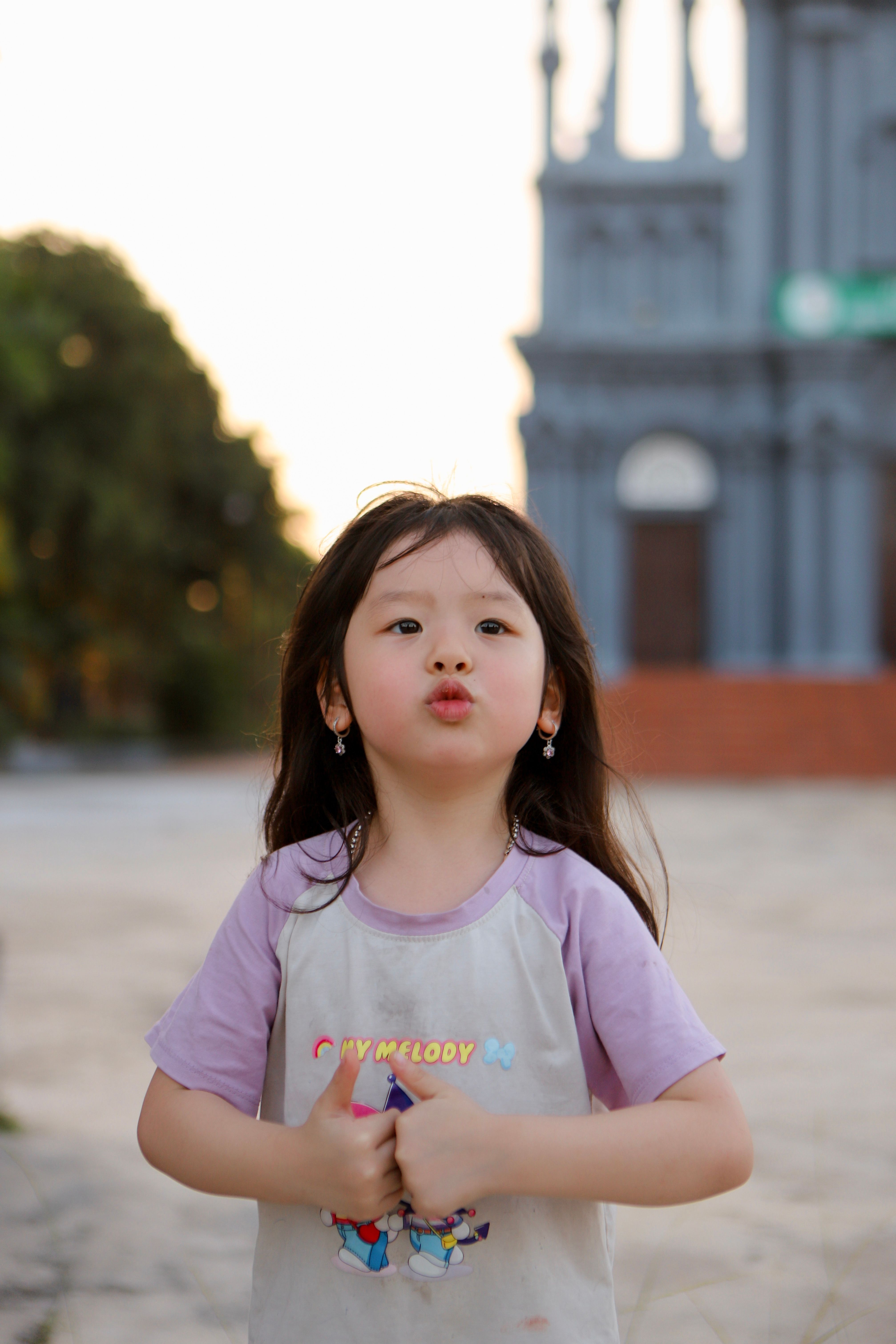 Adorable girl poses playfully outdoors, capturing innocence and charm at twilight in Vietnam.