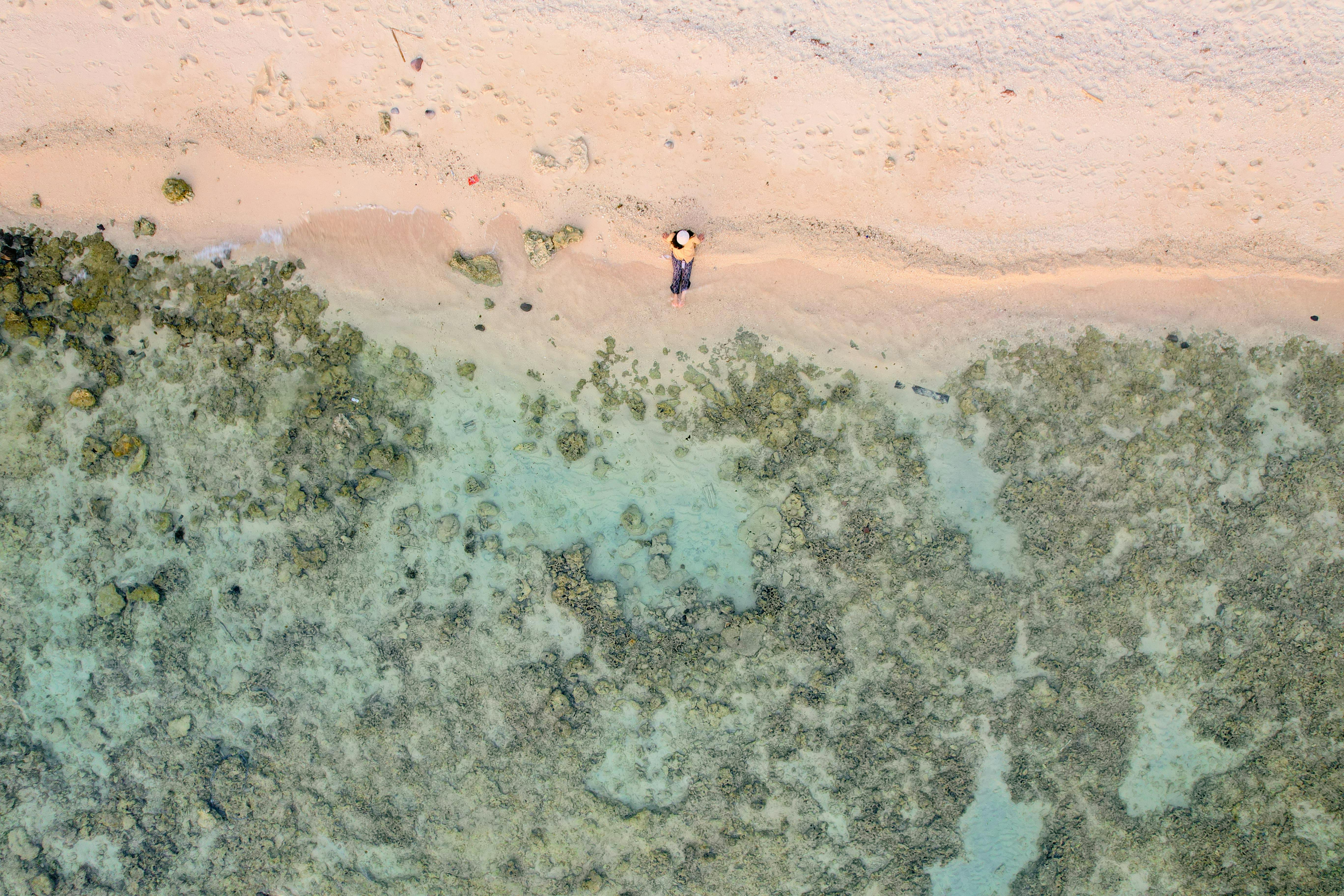 High-angle aerial view of a tranquil beach in South Sulawesi, Indonesia, showcasing clear waters and coral formations.