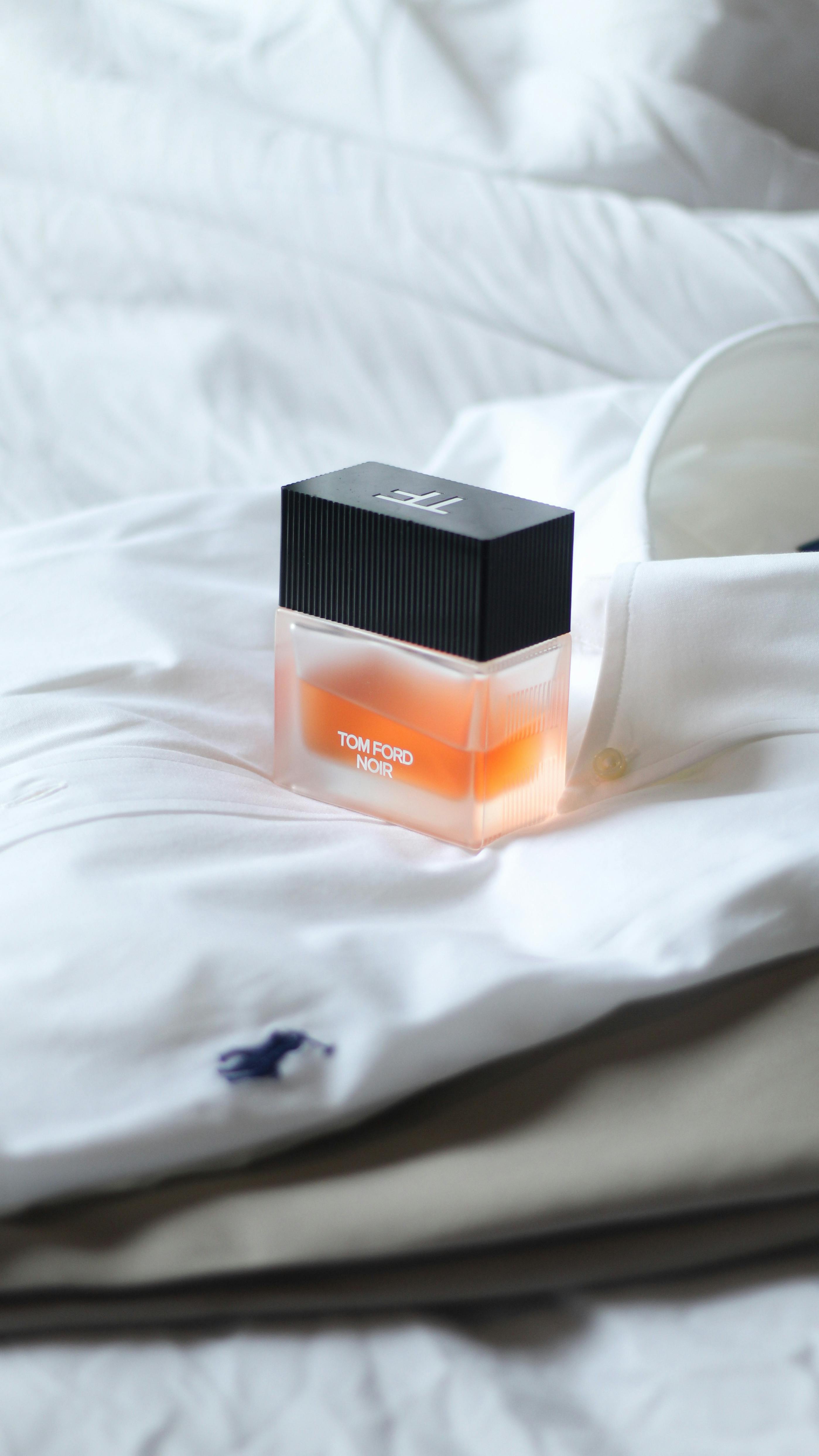 A stylish perfume bottle placed on a crisp, white shirt with folded collar.