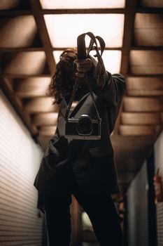 Artistic shot of a woman holding a vintage camera under industrial lighting.