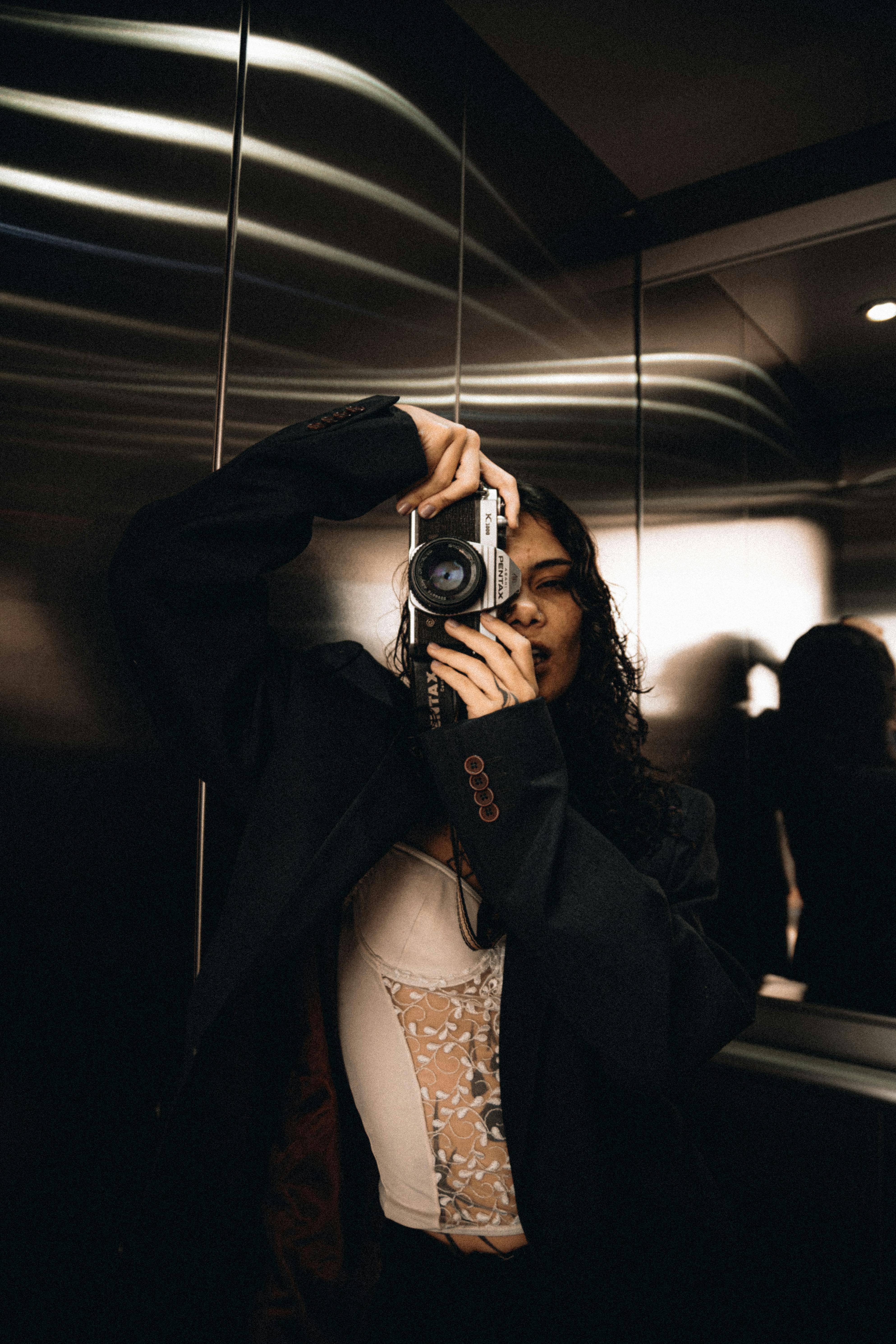 Stylish woman taking a photo with a vintage camera in an elevator with reflective walls.