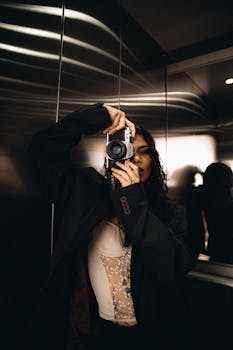 Stylish woman taking a photo with a vintage camera in an elevator with reflective walls.