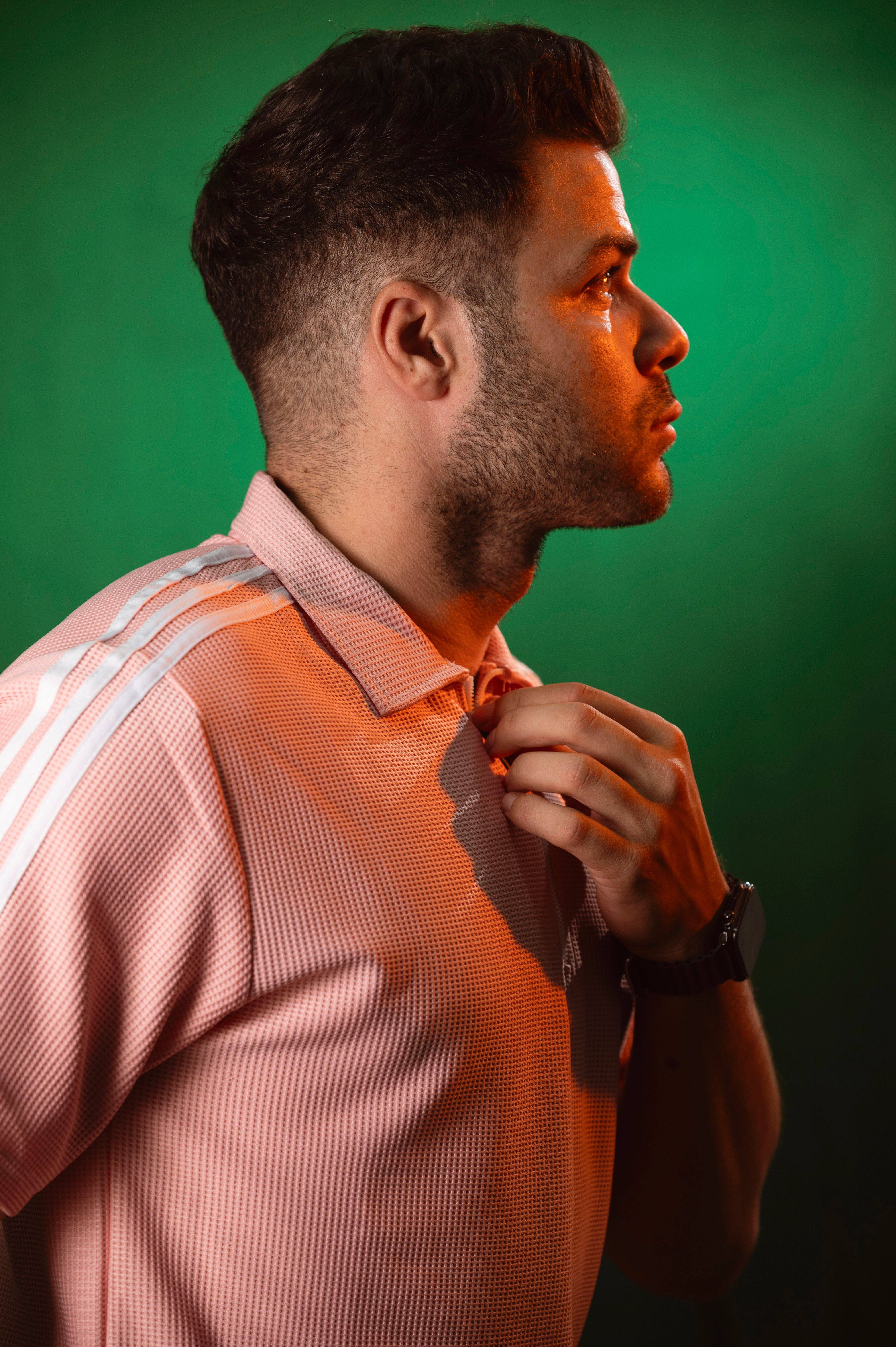 Side profile portrait of a man against a green background, adjusting his shirt collar.