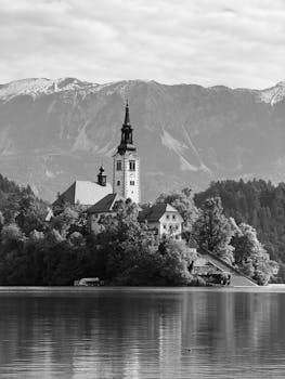 Scenic view of Bled Island with church, surrounded by mountains in monochrome.