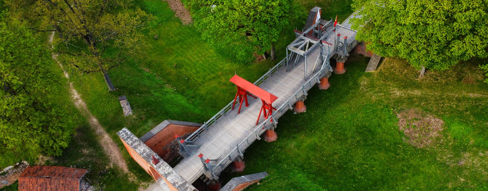 An aerial shot of the historic wooden drawbridge at Biržai Castle, surrounded by lush greenery in Lithuania.