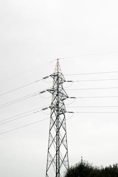 A towering high voltage transmission structure with power lines against a neutral grey sky.