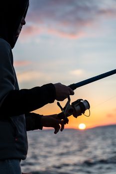 Silhouette of a person fishing by the sea at sunset, capturing a tranquil and scenic moment.