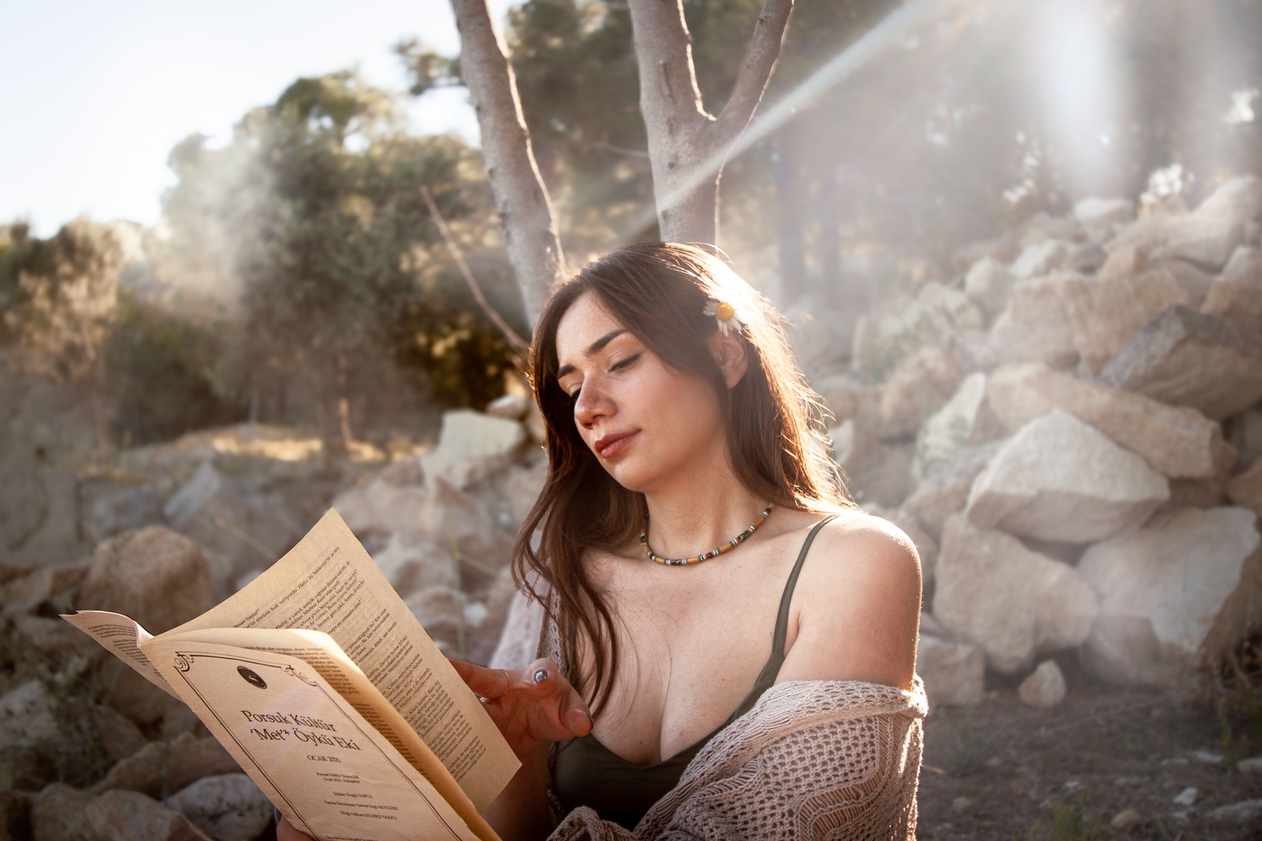 A woman relaxes outdoors, reading in the sunlit Çanakkale forest.