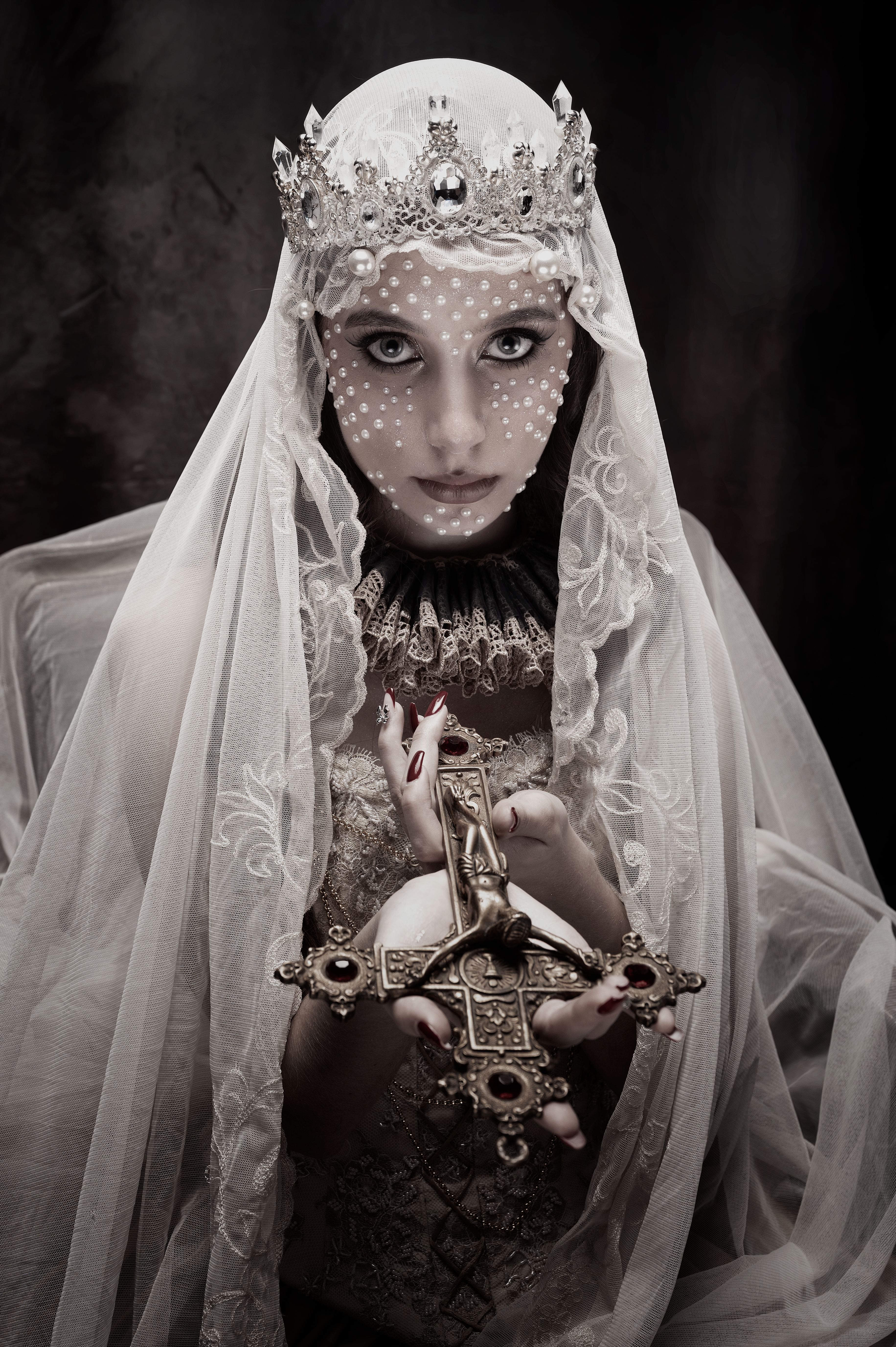 Mysterious woman draped in lace and veil holding an ornate cross.