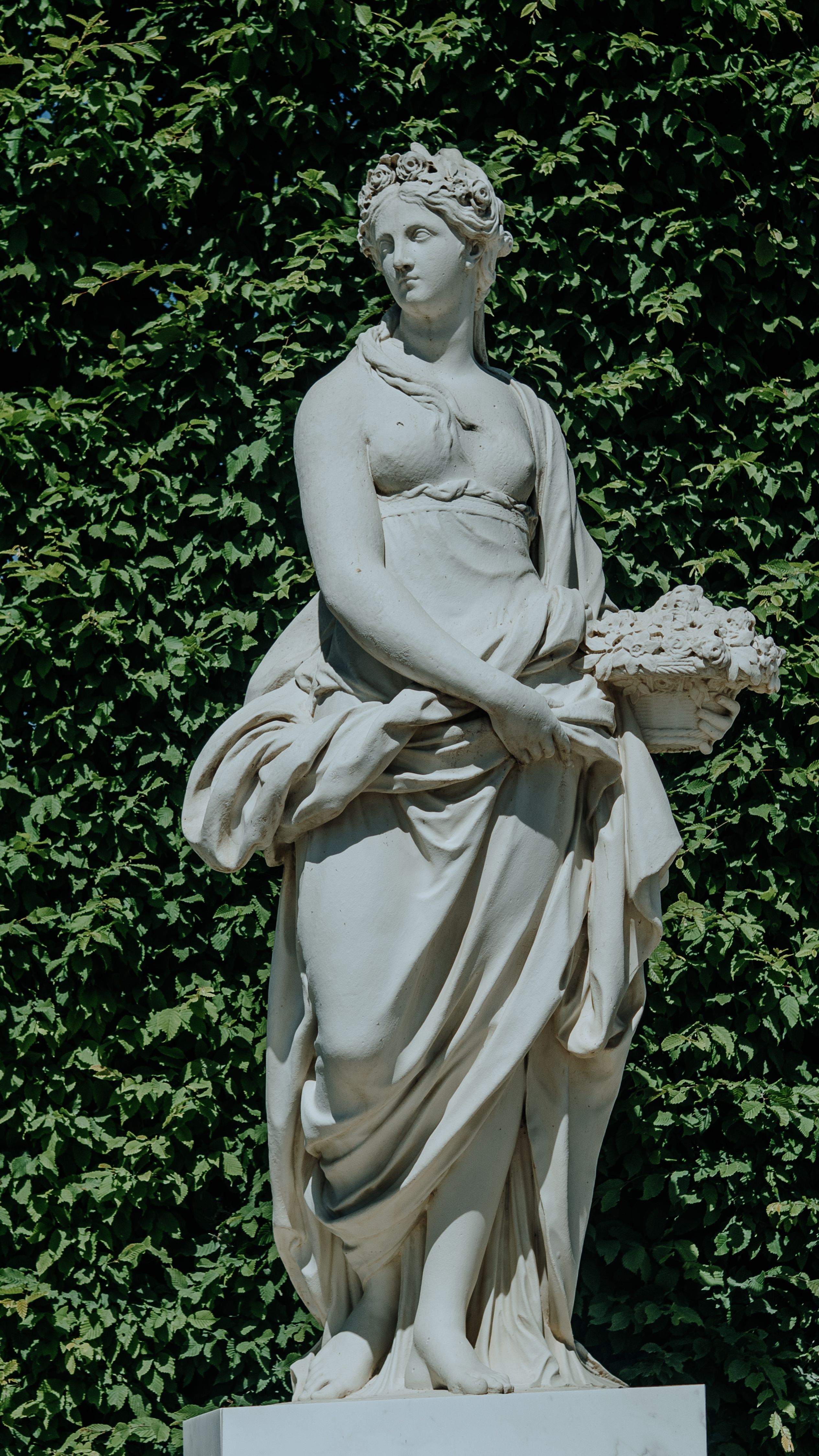 Classical statue elegantly posed against lush greenery in a Parisian garden, showcasing historical artistry.