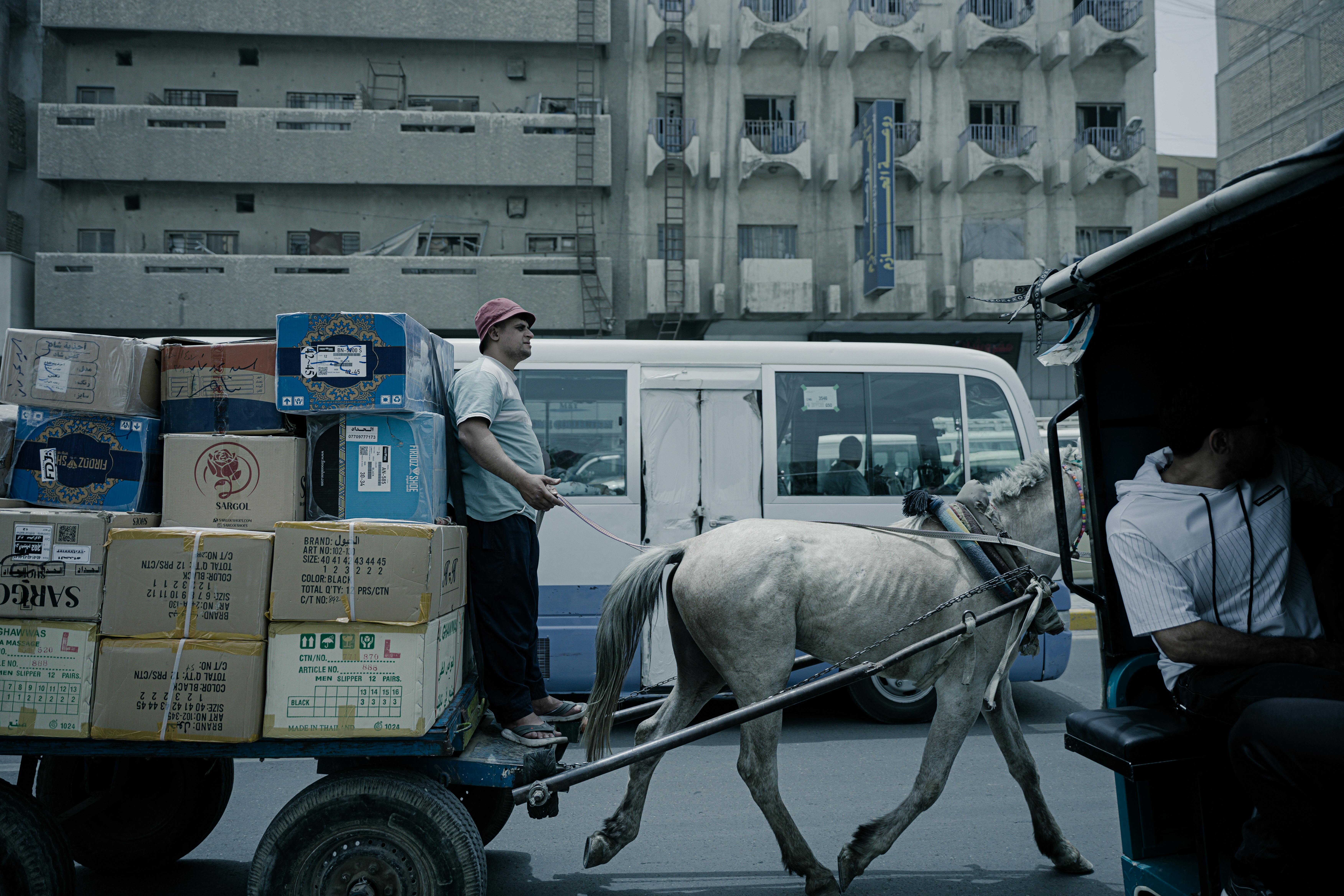 Free Horse-drawn cart carrying boxes in a busy urban street setting. Stock Photo
