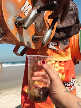A vendor pours chilled mate tea into a plastic cup on a sunny beach day, capturing the essence of Rio de Janeiro street culture.