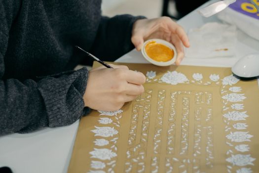 A close-up view of a hand painting intricate floral patterns on paper.