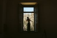 Silhouette of a person standing in a window frame overlooking nature. Captures solitude and reflection.