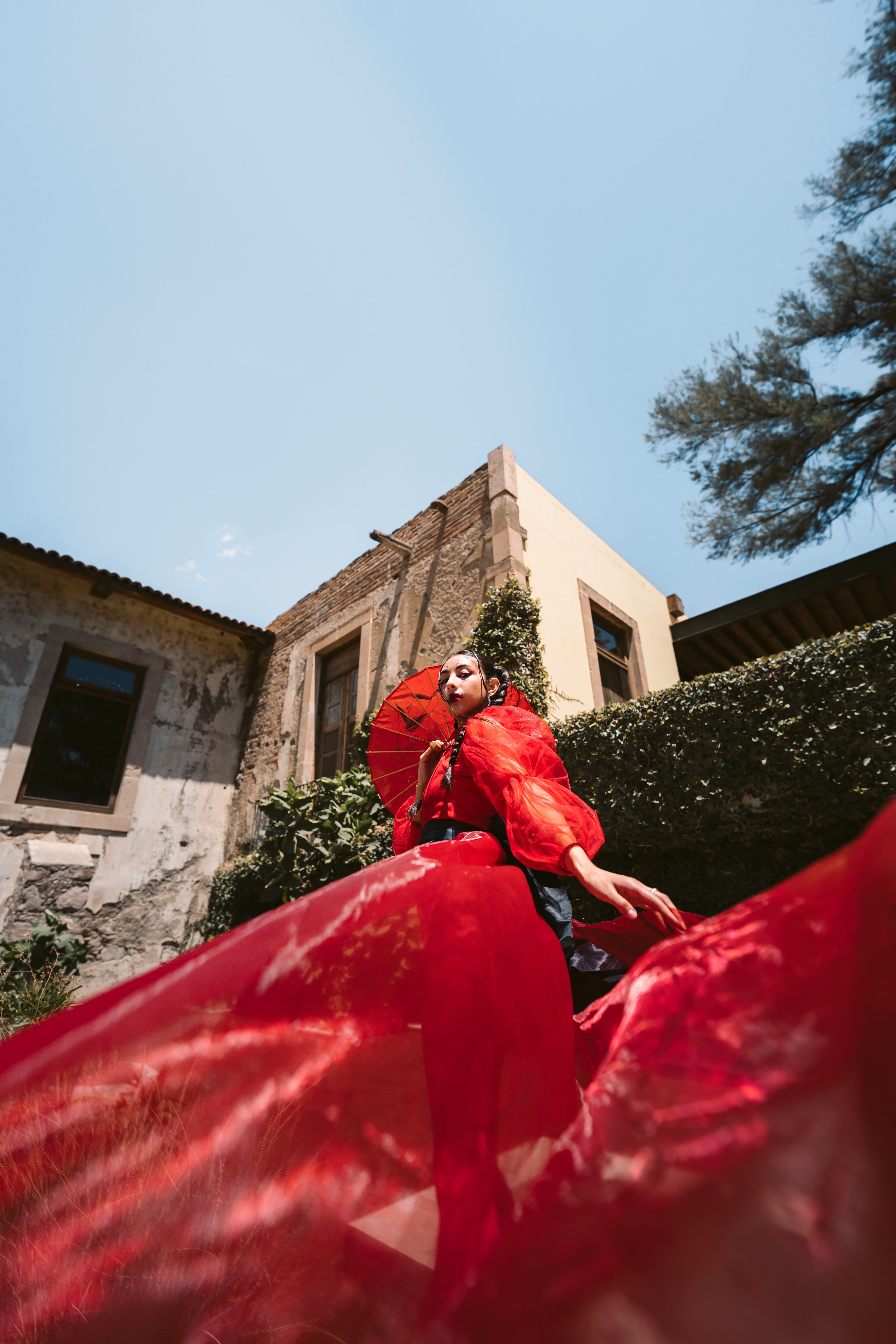 [ColoSach]-a-fashionable-woman-in-a-vibrant-red-dress-holding-a-red-umbrella,-standing-outdoors-against-a-historic-building.