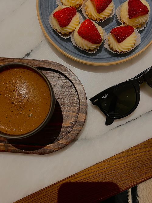 Free A cozy scene with a hot coffee, strawberry tarts, and sunglasses on a marble table. Stock Photo