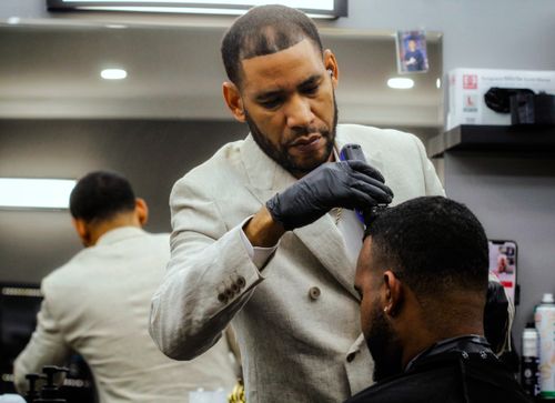 Free A barber in a white suit jacket carefully cuts a client's hair in a modern salon setting. Stock Photo