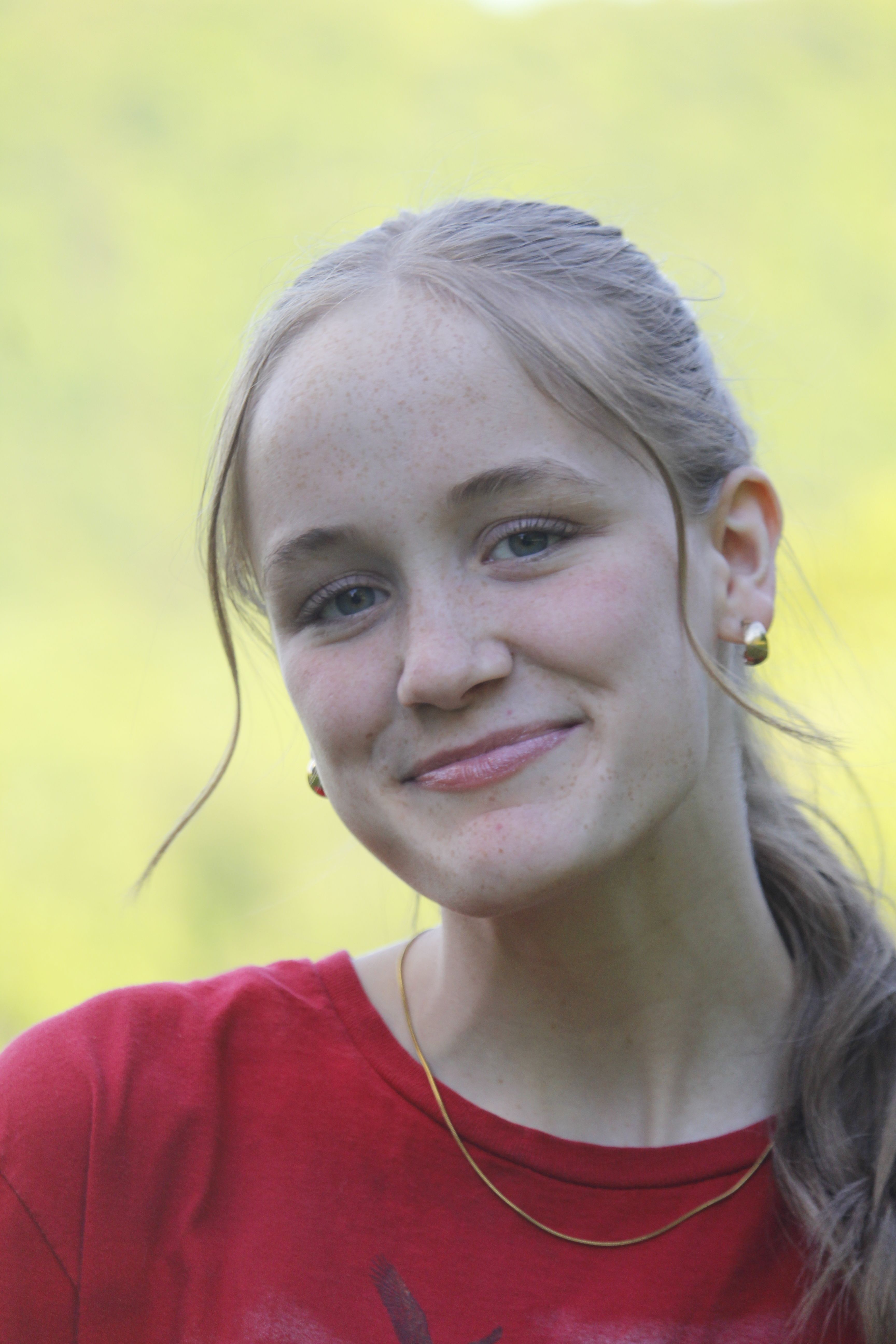 Portrait of a smiling young woman wearing a red shirt in a natural outdoor setting.