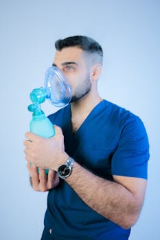 Medical worker in blue scrubs using a respiratory mask, emphasizing respiratory care.