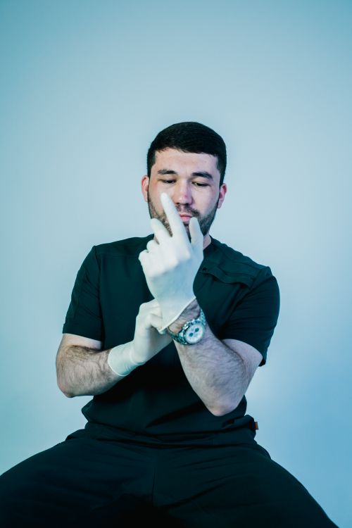Free A male healthcare worker putting on gloves, ensuring hygiene. Ideal for medical concepts. Stock Photo