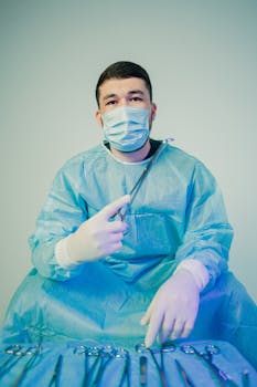 A surgeon in a blue gown and mask, holding scissors, sits behind surgical tools.