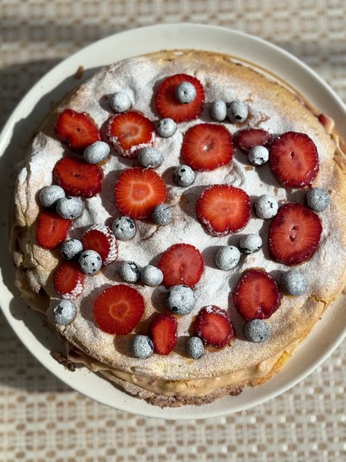 Free Delicious meringue cake topped with fresh strawberries and blueberries, dusted with powdered sugar. Stock Photo