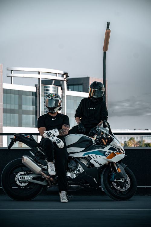 Free Two motorcyclists with helmets on a parked bike in front of modern buildings. Stock Photo