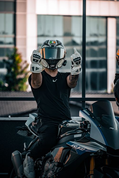 Free Motorcyclist in helmet and gloves shows peace sign on a sleek sport bike outdoors. Stock Photo