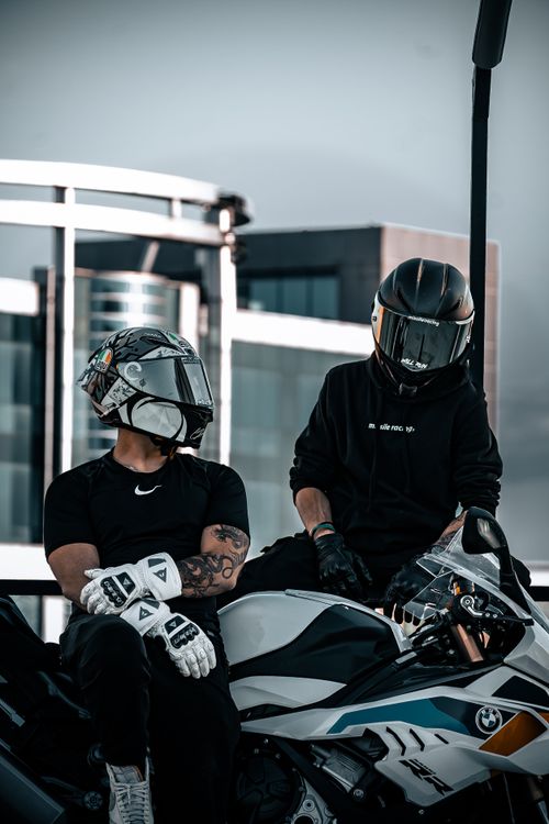 Free Two bikers with helmets resting on a motorcycle in front of modern buildings. Stock Photo