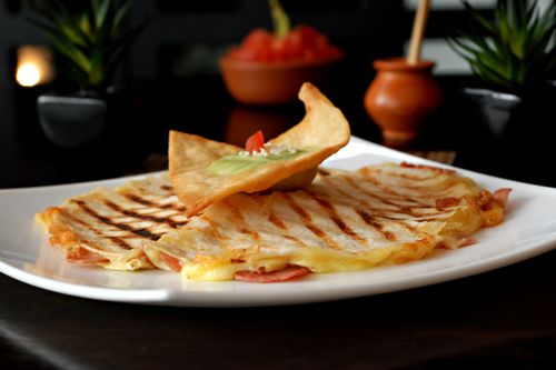 Free Tasty grilled quesadilla topped with guacamole and salsa, served in a cozy Mexican setting. Stock Photo